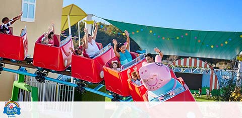 People on a Peppa Pig-themed roller coaster raising their arms joyfully.