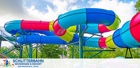 Vibrant water slides twist and turn at Schlitterbahn Waterpark and Resort, New Braunfels, Texas. The colorful tubes in blue, green, yellow, and red are set against a backdrop of trees and a partly cloudy sky, promising fun and excitement.