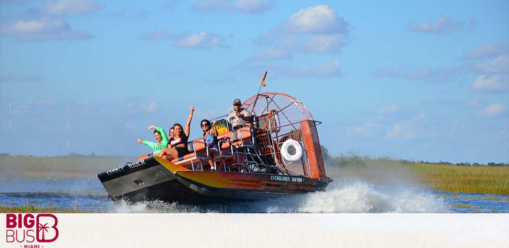 Airboat with tourists glides on water amidst grassy landscape.