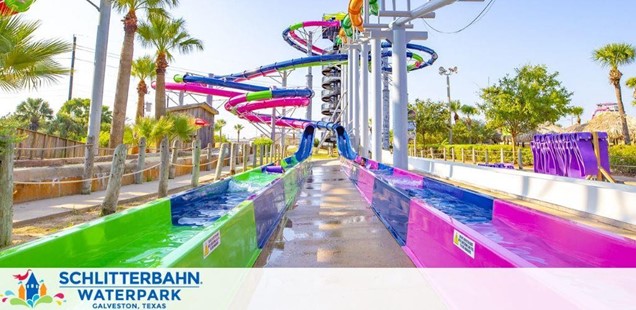 Image shows a vibrant, multicolored waterpark slide setup at Schlitterbahn Waterpark Galveston, Texas. Placid waters rest at the slide base surrounded by palm trees under a clear blue sky, inviting a joyful escape from the everyday.