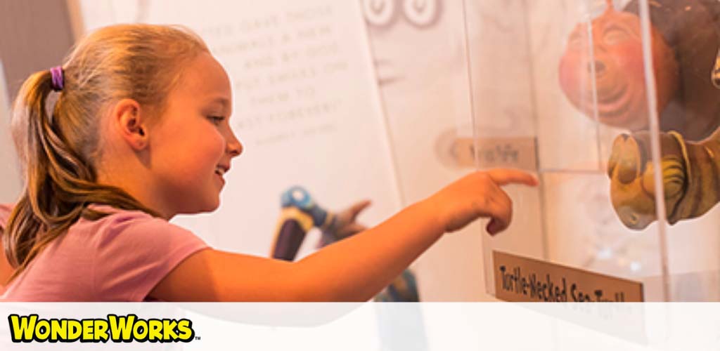 A girl smiling, pointing at an exhibit inside WonderWorks.