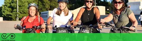 Four smiling people on bicycles under a clear sky.