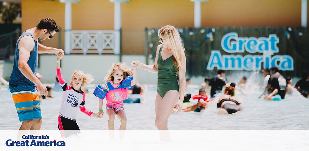 This image captures a joyful moment at California's Great America amusement park. A man and two children, perhaps a father and his kids, are holding hands and playing in a shallow wave pool. The kids are wearing sun-protective swimwear with bright colors and smiling widely. On the right, a woman stands in profile, watching the scene, dressed in a one-piece swimsuit. The background is slightly blurred, focusing on the action in the forefront, and features the "Great America" sign behind a faux-architecture façade. The picture conveys a sense of family fun and summertime leisure at the park.

Experience the excitement and make memories without breaking the bank; visit GreatWorkPerks.com for the lowest prices and biggest savings on tickets to great destinations like California's Great America.