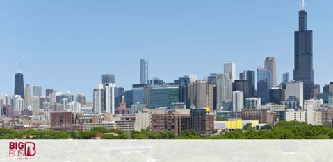 The image features a panoramic view of a city skyline on a clear day. Skyscrapers dominate the center, with a notable tall tower rising above the rest. Trees and smaller buildings are in the foreground, and the sky is bright blue. A logo with the text  Big Bus  is visible in the bottom left corner.