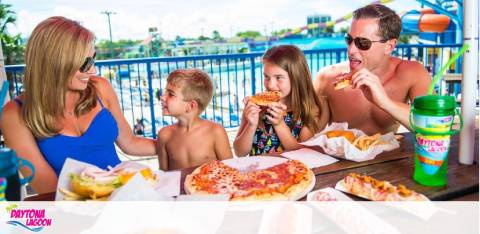 A happy family enjoys pizza together at an outdoor table.