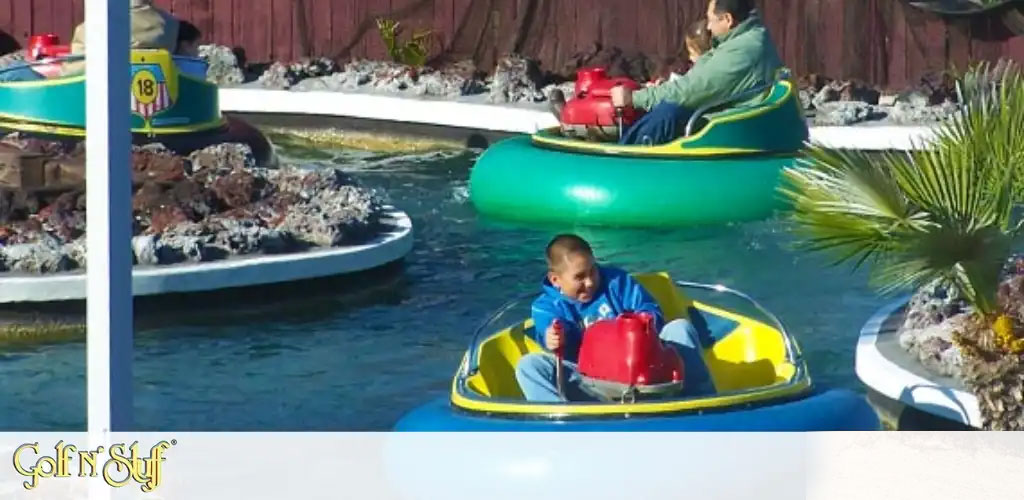 This image captures a vibrant outdoor scene featuring a water-based amusement ride at "Golf N' Stuff". In the foreground, a young child, wearing a blue shirt and concentrating intently, steers a colorful red and blue bumper boat through the clear blue water. Additional bumper boats, each ridden by an individual enjoying the experience, navigate the surrounding waters with rocky landscaping and a small palm tree in the background, which adds to the tropical vibe of the setting. The bright sunlight enhances the cheerful atmosphere of the recreational activity.

At GreatWorkPerks.com, we offer the lowest prices, ensuring you get the best savings on tickets so you can enjoy moments like these without breaking the bank.