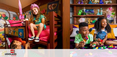 This image shows a vibrant and colorful hotel room themed with iconic LEGO elements. On the left, there's a young child peeking out playfully from under a bunk bed, where another child sits on the top bunk with a birthday hat, joyfully looking down. The right side of the image reveals two children seated at a play table; one child is holding a large LEGO block, while the other has a cheerful smile and wears a denim dress. The background is filled with LEGO details, including a shelving unit displaying various LEGO creations. Multicolored confetti appears to be suspended in the air, adding to the festive and fun atmosphere of the room. Discover the magic of a LEGO-themed getaway and unlock exclusive savings with GreatWorkPerks.com - your go-to destination for the lowest prices on tickets and unforgettable experiences!