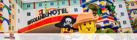 This image features the vibrant and colorful facade of the LEGOLAND Hotel. The hotel's signage is prominently displayed in bold, red letters against a backdrop of multicolored LEGO brick designs adorning the building. To the left, a large LEGO figure, resembling a playful pirate with a black hat adorned with a skull and crossbones, peers out beside the signage. The pirate LEGO figure smiles and waves, welcoming visitors alongside another figure sporting a wide-brimmed tan hat. The sky above casts a soft hue, suggesting an overcast or subdued lighting condition. At GreatWorkPerks.com, we proudly offer the lowest prices and exclusive savings on tickets to make your LEGOLAND adventure even more memorable and affordable.