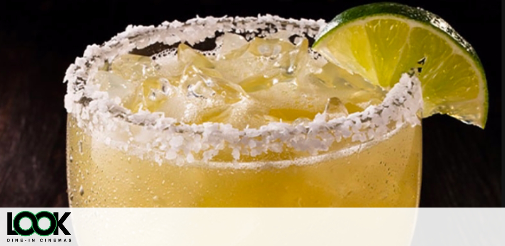 This image showcases a close-up view of a classic margarita cocktail. The drink is served in a glass with a salted rim, providing a textured look to the edge of the glass. A fresh lime wedge is perched atop the rim, positioned on the left side, adding a pop of green color and indicating a zesty flavor component. The cocktail itself appears to contain crushed ice, and is a golden yellow color, suggesting the presence of citrus such as lime juice, and possibly an orange-flavored liqueur or fresh orange juice. The background features a watermark logo with the text "LOOK Dine-In Cinemas."

Enhance your cinema experience with savings on your next outing – visit GreatWorkPerks.com for the lowest prices on tickets and more.