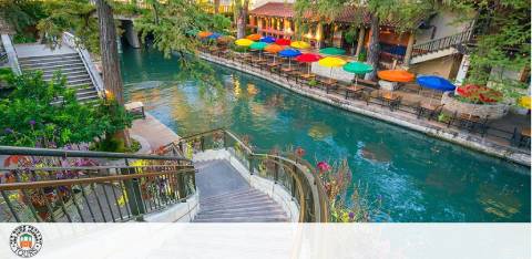 Stone stairs lead down to a canal flanked by colorful umbrellas and greenery.