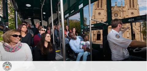 Passengers on a tour bus with a view of a historic church and a driver.
