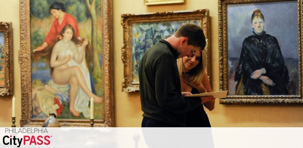 A couple closely observes a brochure inside an art gallery. Classic framed paintings, including portraits and a reclining nude, adorn the wall behind them. The room is warmly lit, enhancing the rich colors of the art. The Philadelphia CityPASS logo is visible in the corner, suggesting discounted entry to attractions.