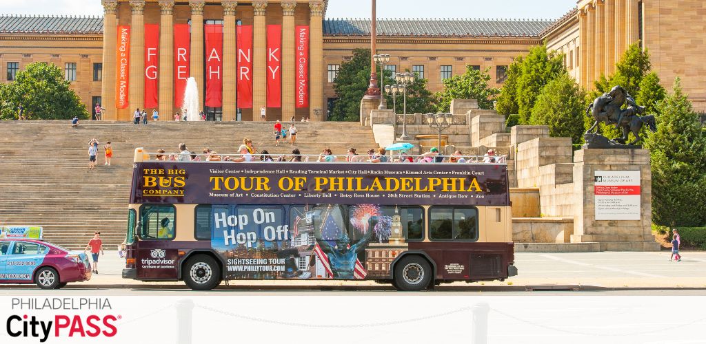 Image depicts a sightseeing bus in front of the iconic steps of the Philadelphia Museum of Art, with banners and a statue visible. People are seen on the steps and walking nearby. The bus promotes hop-on hop-off tours.  Philadelphia CityPASS  is shown at the bottom.