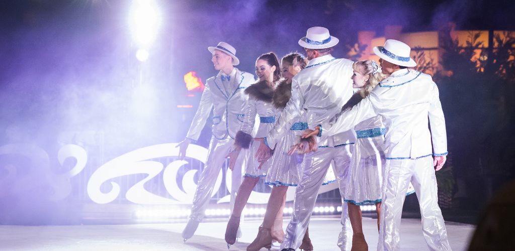 A group of dancers in white outfits performing on stage, showcasing synchronized movements and expressions.