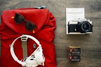 Foto aérea de uma mochila, óculos, fone de ouvido, camera, documentos e filme sob uma mesa. Photo via Visual hunt