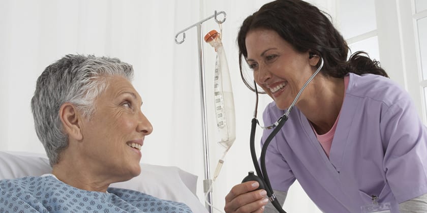 Happy female patient in bed and nurse with stethoscope