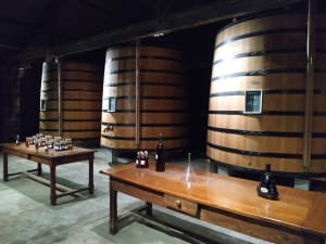 Large wooden vats behind tasting tables with bottles and samples in a Cognac distillery