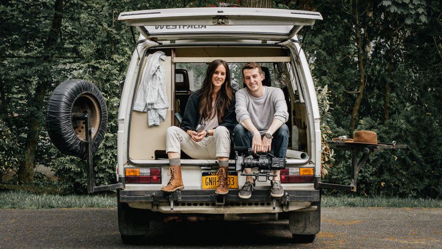 Couple posing in van with their camping and photography equipment
