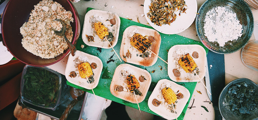 Plates of grilled street corn sit on plates with various toppings in bowls