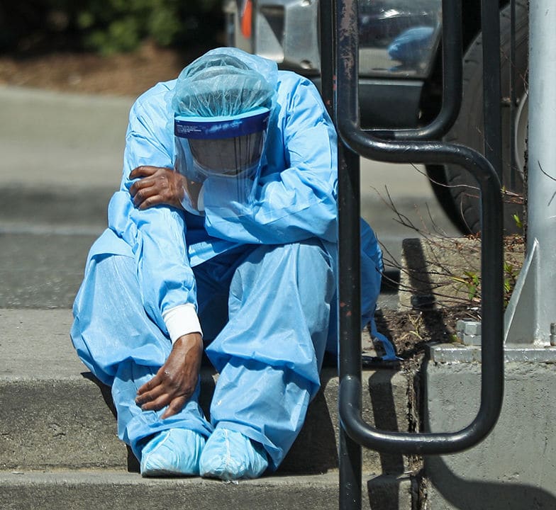 Medical person in scrubs and PPE, slumped on steps.