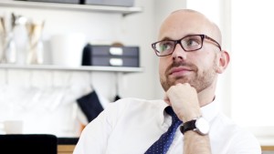Oscar Ohlis är en av Vegas sommarpratare 2014 Oscar Ohlis, en av vegas sommarpratare 2014 blickar bakåt, ser fundersam ut, klädd i kragskjorta och slips i ett vitt rum