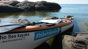 En kajak vid en stenig strand. Kajaken har texten #blåvitabandet.