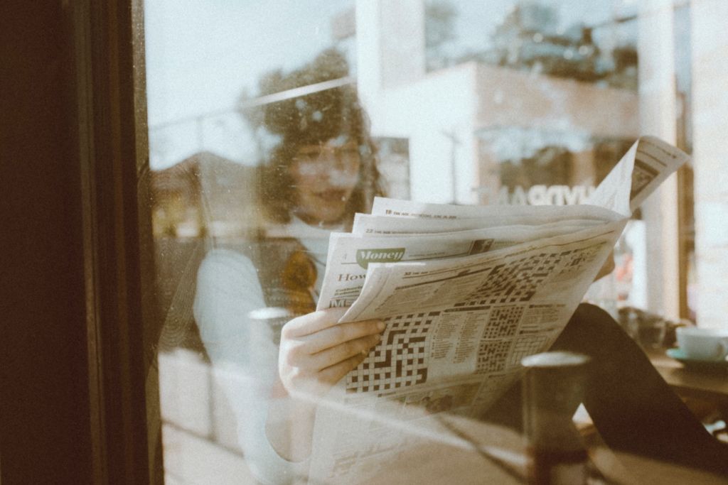 Photo of a woman reading a newspaper, taken through a window