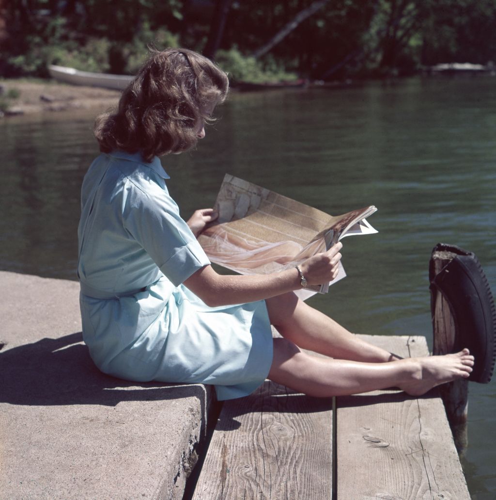 Vintage photo of a woman sitting on a dock reading a newspaper