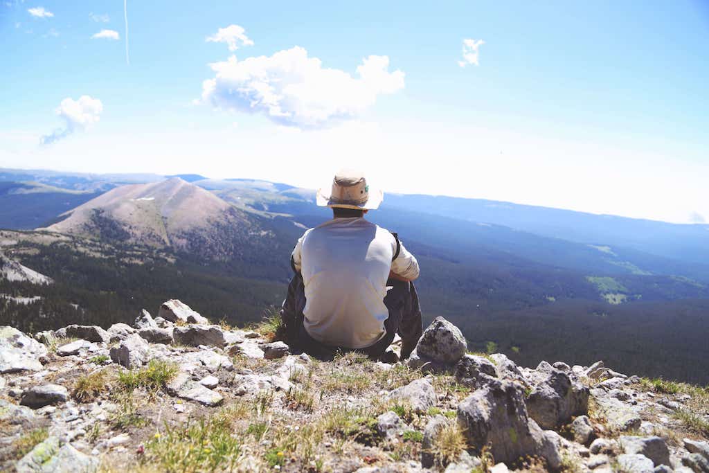 dude sitting on top of a mountain overlooking a valley, looks like someone who probably does some freelancing