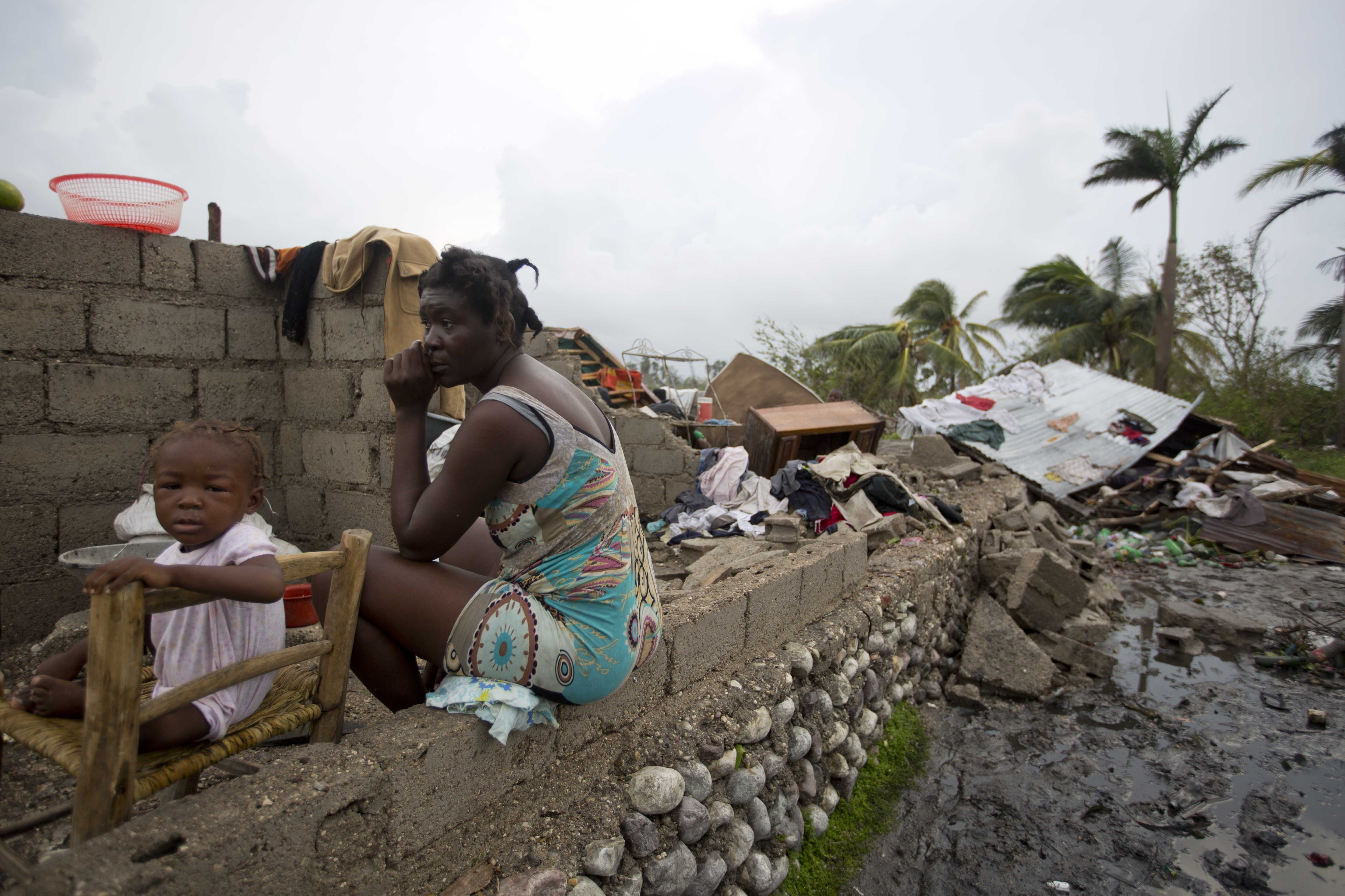 Victor Farah and her daughter sit in the ruins of their home destroyed by Hurricane Matthew in Les Cayes, Haiti, Thursday, Oct. 6, 2016. Two days after the storm rampaged across the country's remote southwestern peninsula, authorities and aid workers still lack a clear picture of what they fear is the country's biggest disaster in years.