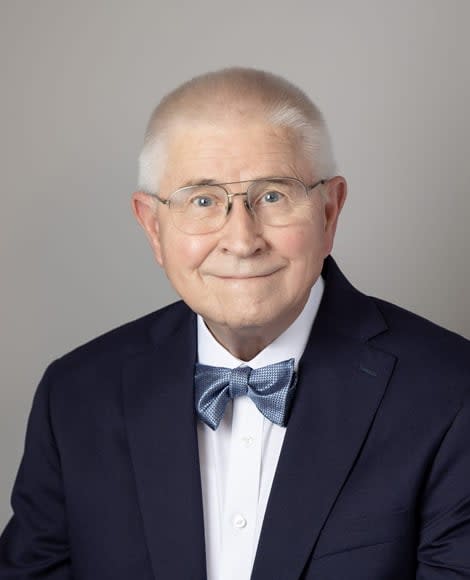 Dr. Creighton in a suit jacket with a blue bow tie smiling supportively.