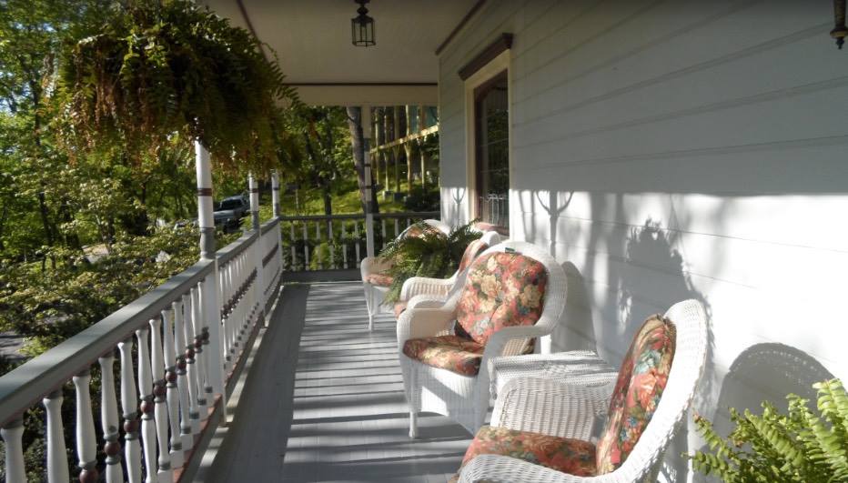 Shows the front porch of the Inn with hanging ferns and White wicker chairs