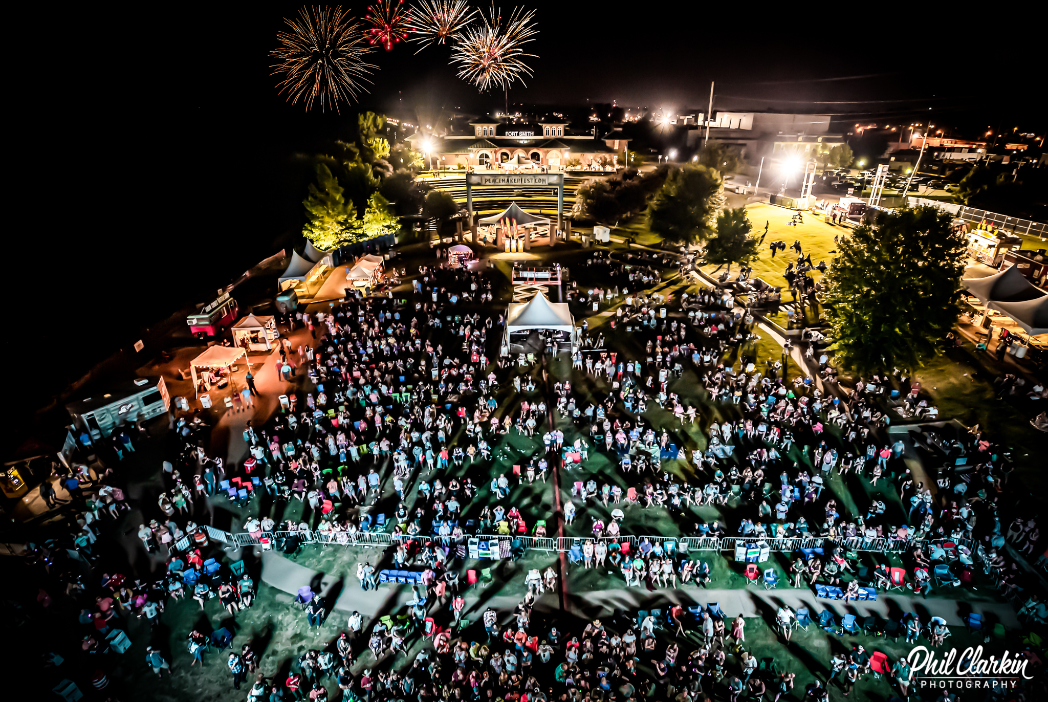Aerial shot of large crowd in front of music stage with fireworks overhead.