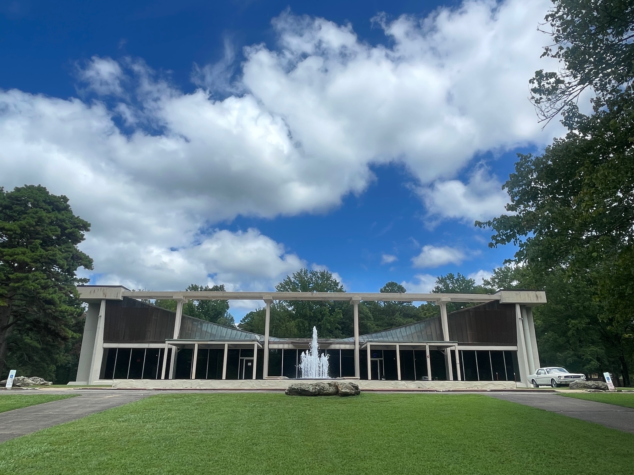 Large building with fountain out front and a green lawn under a blue sky with clouds.