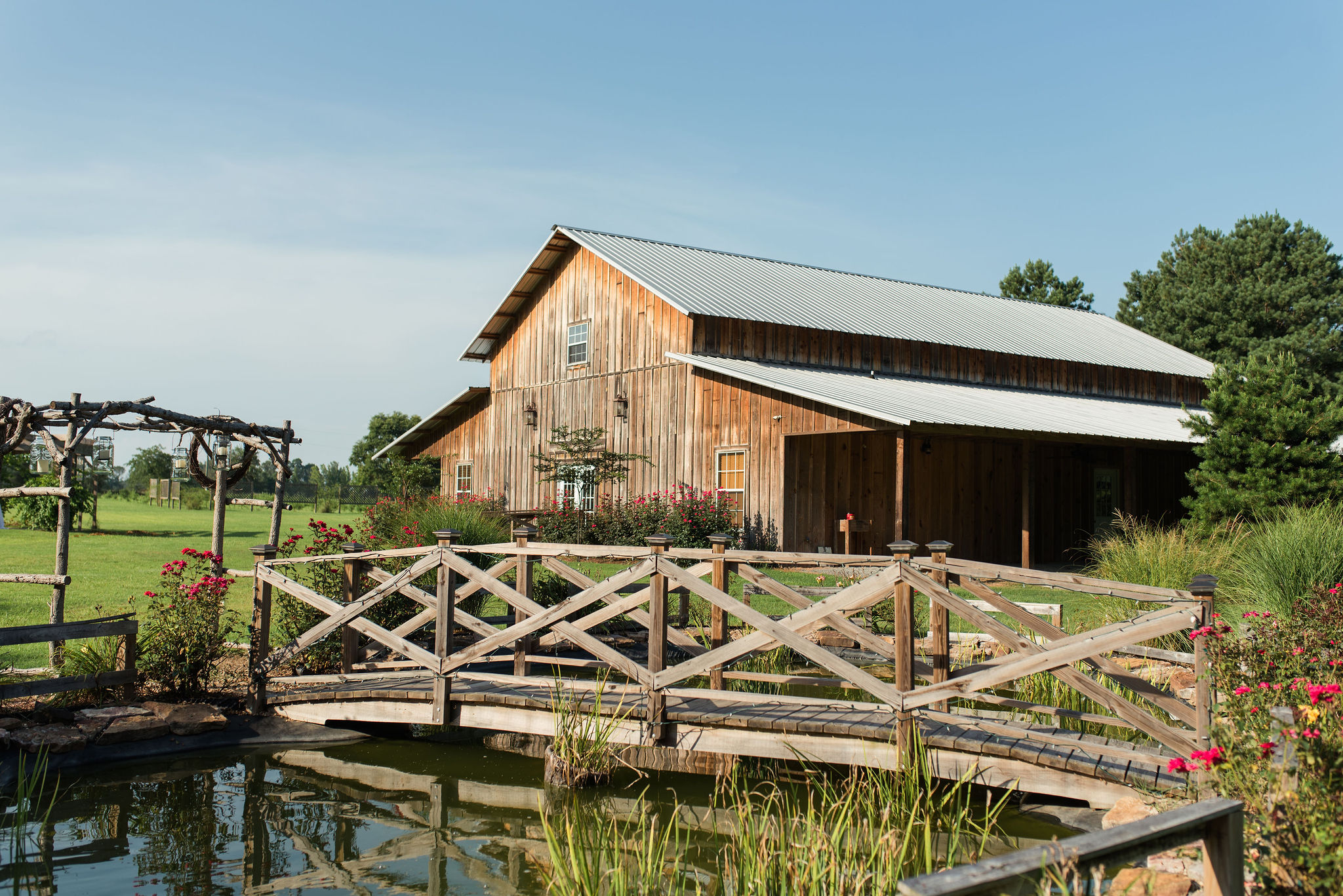 View of a large beautiful wooden barn behind a wooden bridge over a stream.