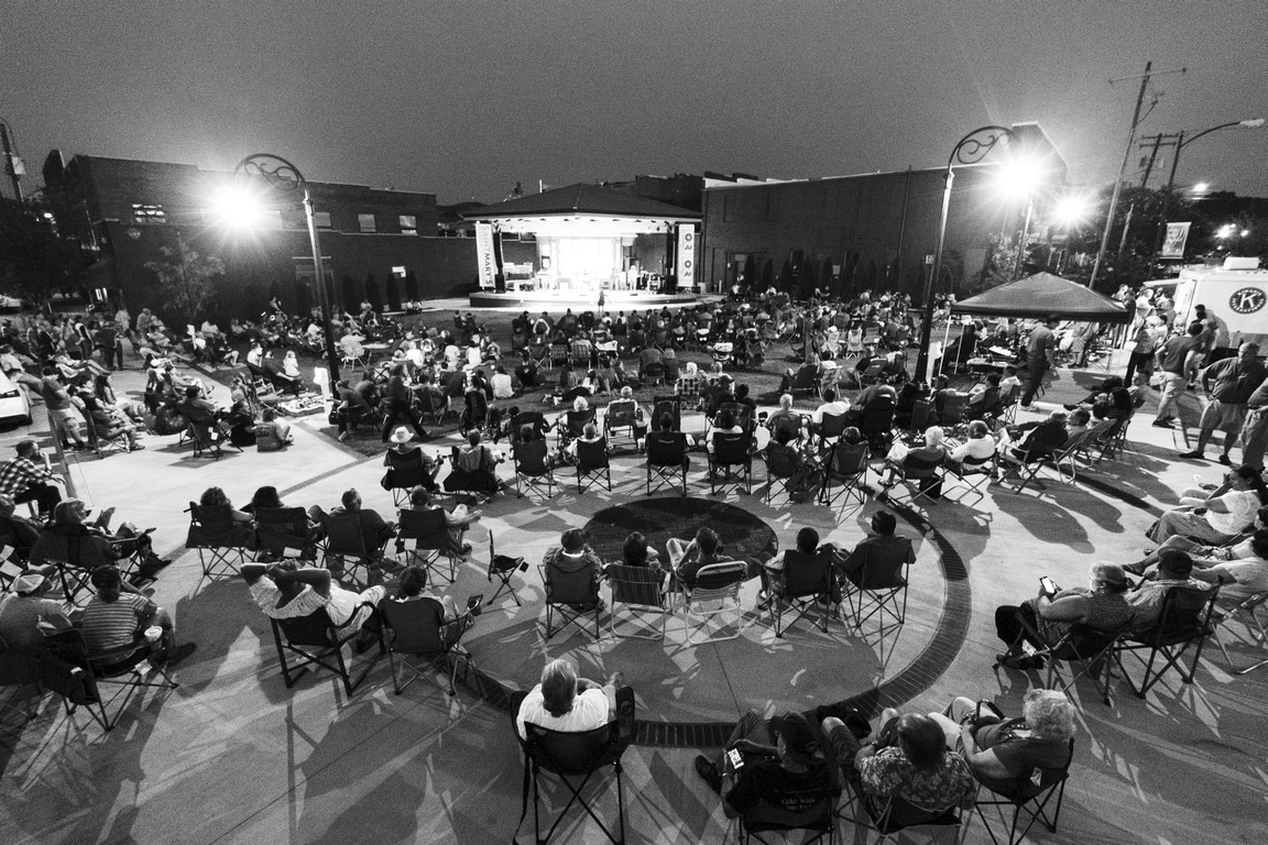 Black and white aerial view of large crowd gathered around outdoor stage.