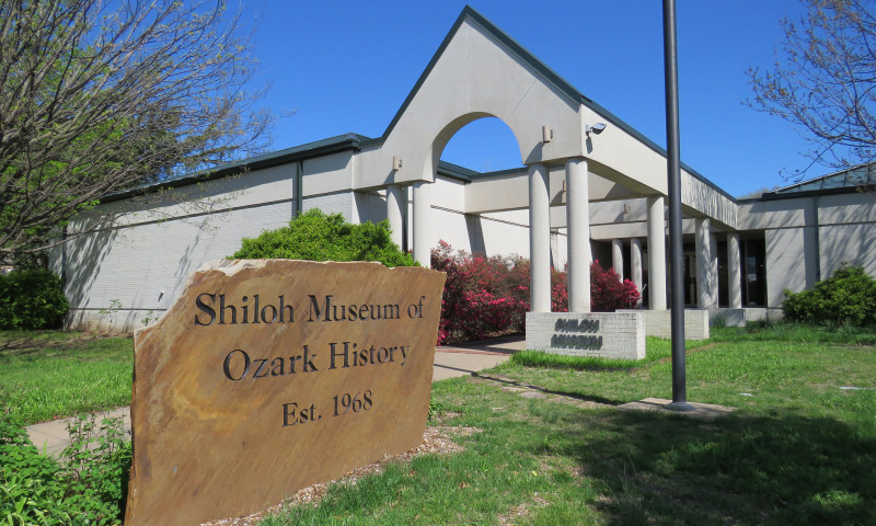 Entrance of the Shiloh Museum of Ozark History with a large, flat stone with "Shiloh Museum of Ozark History, Established 1968" engraved on it.