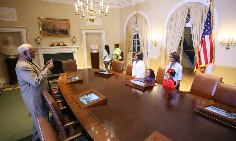 A family poses for photos inside the Clinton Presidential Center's Cabinet Room exhibit