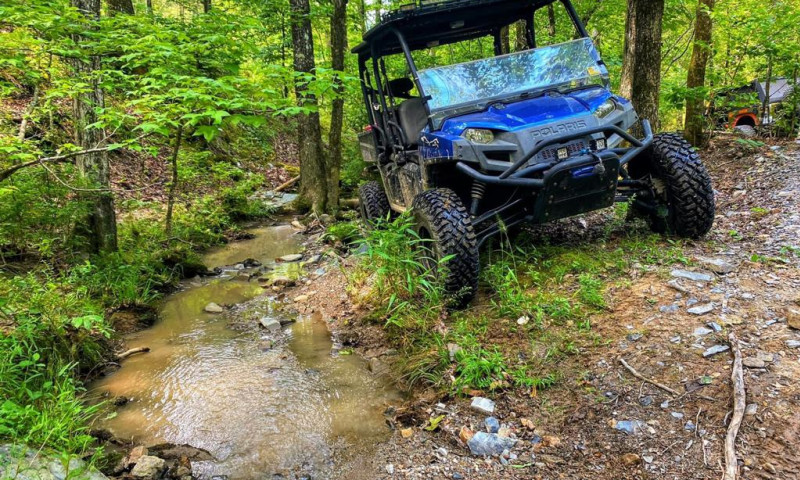 Blue ATV parked beside small creek in a dense green forest.