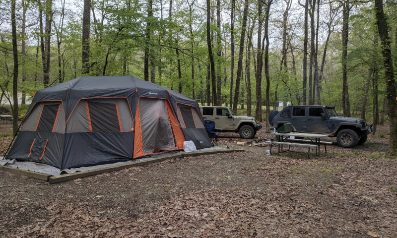 Large grey tent at campsite in woods, with two Jeeps parked behind.