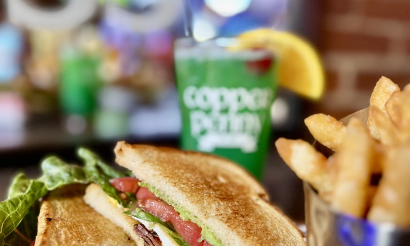 Sandwich cut in half, with fries, and a green drink in a pint glass.