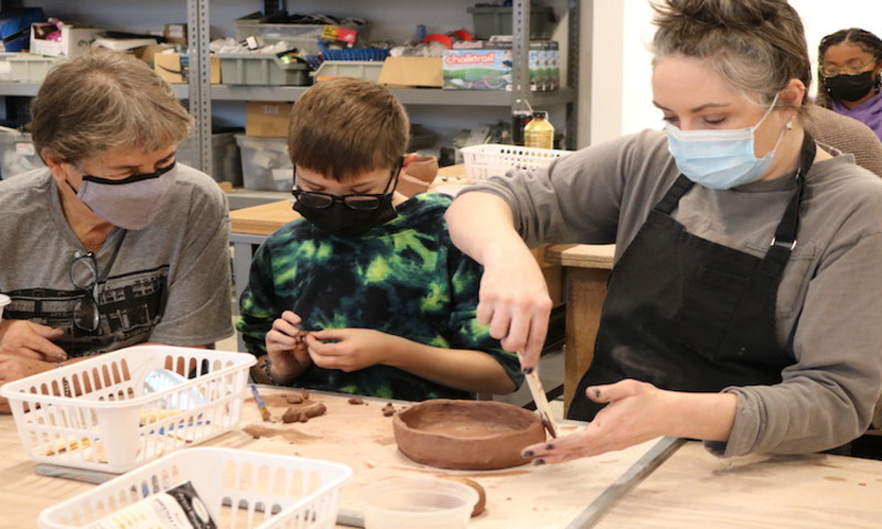 Two women and a boy sculpt pottery from clay at a worktable. 