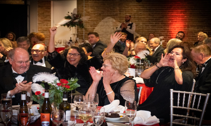 A group of people dressed in cocktail attire sit at lavishly decorated tables in one of the event 