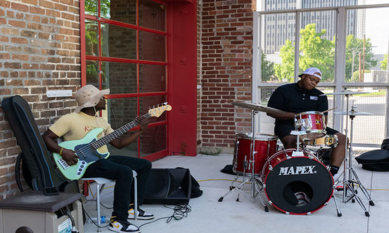 Two musicians playing the drums and the electric guitar outside on the ASC patio. 