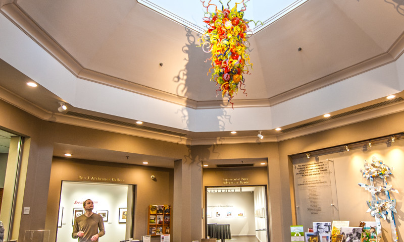 A man looks up to a glass sculpture of multiple colors and shapes that hangs from the ceiling.