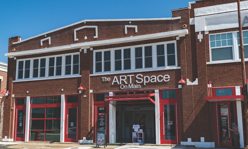 The exterior of ART Space on Main is in a brick building with large windows and red and white trim.