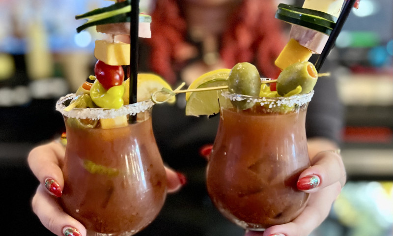 Female bartender holds two Bloody Mary cocktails with garnish.