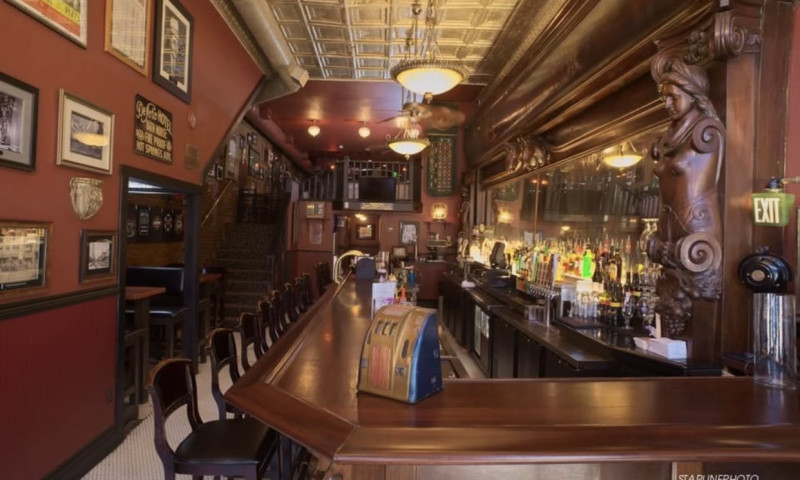 Empty barstools lined up along a massive hand carved bar.