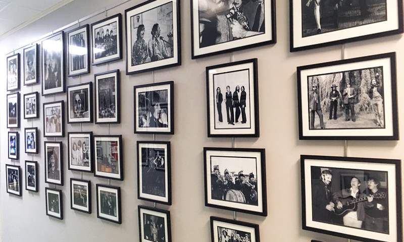 A wall is filled with framed photos of the Beatles. Some feature individual band members, others a combination of members, and some images feature the entire band. Members are featured in a variety of outfits and locations. 