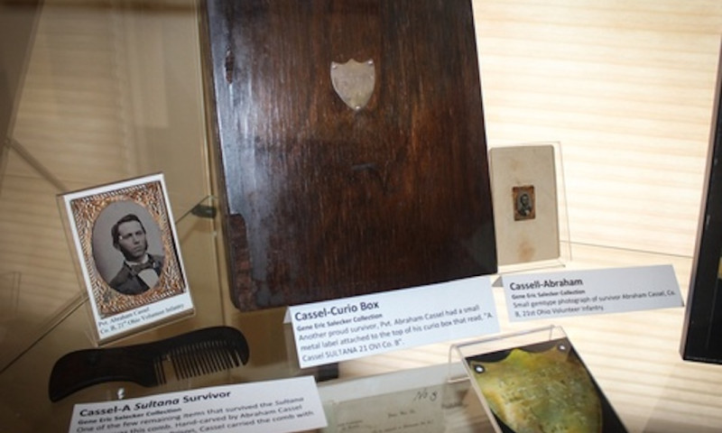A collection of artifacts is on display including Civil War photos and a curio box belonging to Private Abraham Cassel, labeled as a Sultana survivor. 